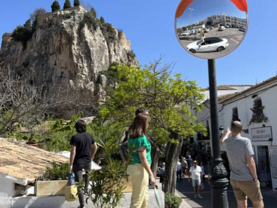 Scenic mountain village street with tourists and a reflective mirror on a lamp post.